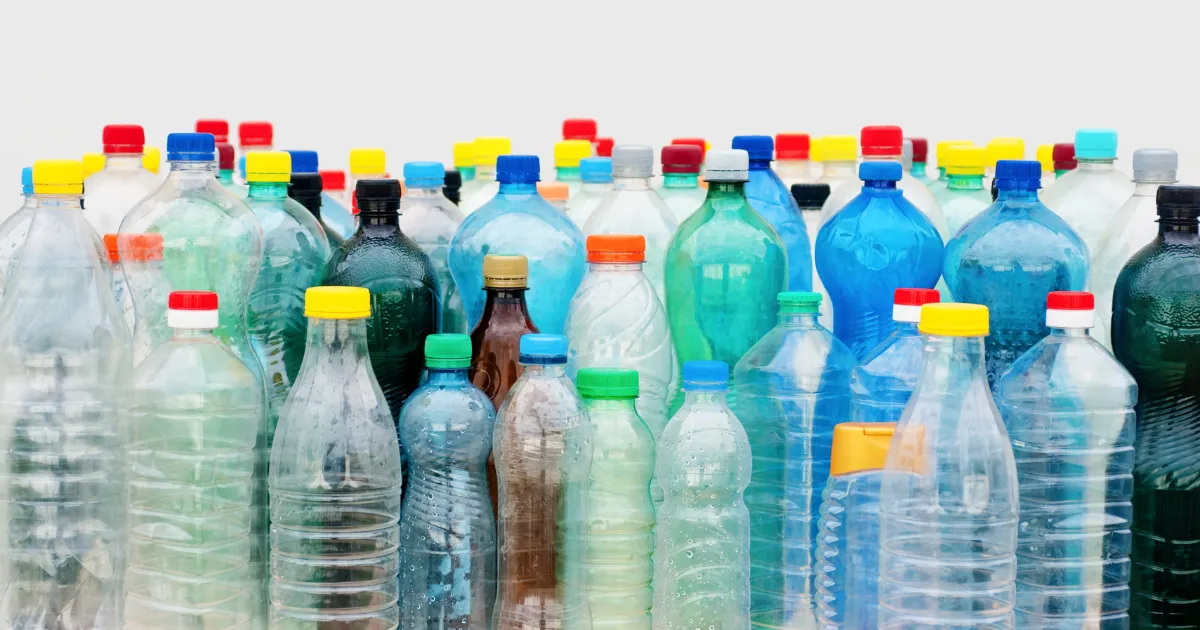 Coleção diversificada de garrafas PET vazias e limpas de vários tamanhos e cores, incluindo transparentes, azuis, verdes e marrons, com tampas coloridas em vermelho, amarelo, azul e verde, organizadas juntas contra um fundo branco neutro.